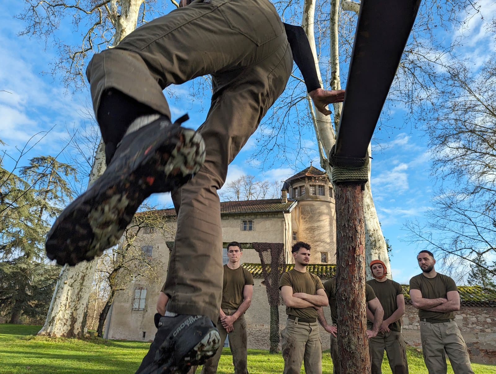 Stagiaire grimpant à la corde le long d'un arbre, encouragé par le groupe